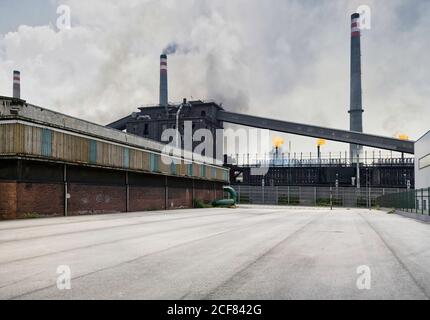 Weathered industrial buildings and pipes emitting smoke and flames at coking factory Stock Photo