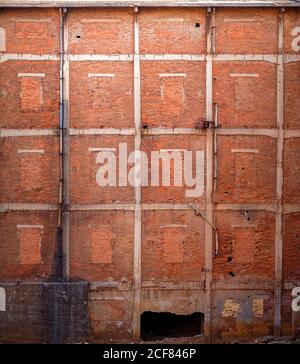 Shabby old high wall of abandoned red brick building with brick windows ruined entrance and pipes with dirty black smudges Stock Photo