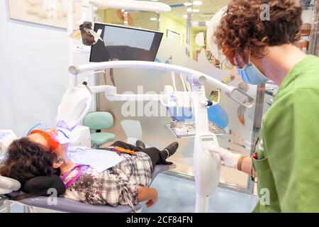 Doctor in uniform preparing equipment for taking x-ray during tooth filling while patient lying in chair in dentistry Stock Photo