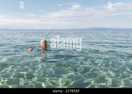 Elderly retired man floating in crystal water enjoying tropical weather being on vacation, Greece