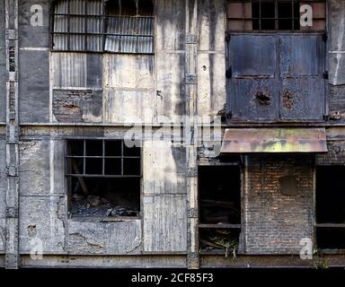 Exterior of old neglected industrial building with crumbling brick walls and damaged windows with metal grids in Asturias in Spain Stock Photo
