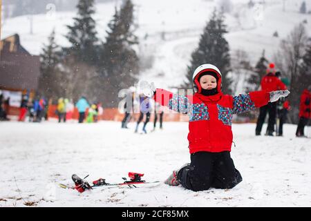Little cute boy with skis and a ski outfit. Little skier in the ski resort. Winter holidays. Skiing Stock Photo