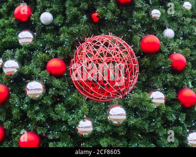 A red wicker ball entwined with a garland hangs among the spruce branches with small red and silver balls around Stock Photo