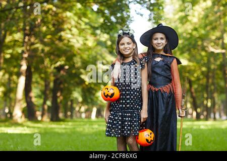 Portrait of two girls in witches costumes smiling at camera while standing in the park outdoors Stock Photo