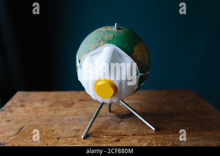 Creative little globe with facial protection respirator masks placed on wooden table against dark blue wall illustrating concept of protection from coronavirus pandemic Stock Photo