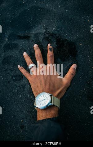 From above hand of anonymous man with ring and watch touching black dirt in countryside Stock Photo
