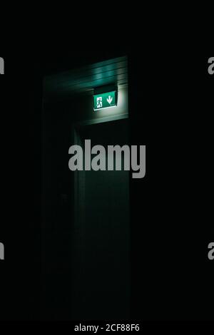 Green exit sign shining over closed door in dark room Stock Photo