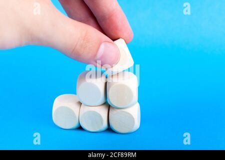 Hand building stairs from small wooden cubes, dice. Putting a final, top element to a simple structure. Going up advancement growth and going forward Stock Photo