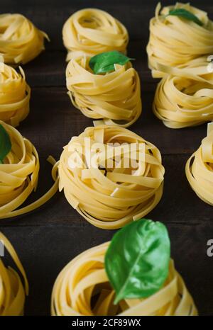 From above arranged pasta nests with fresh basil leaves on wooden kitchen table Stock Photo