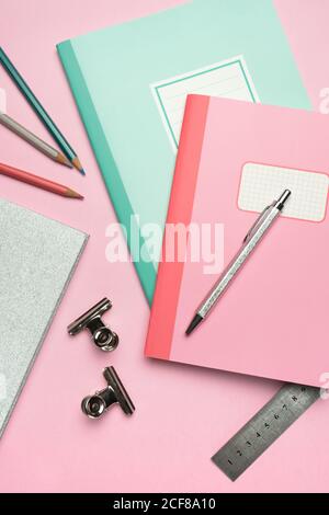 From above composition of colorful notebooks, pen, pencils, ruler and paper clips arranged on pink desk Stock Photo