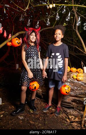 Portrait of two friends in costumes standing and holding hands at the Halloween party in the dark Stock Photo