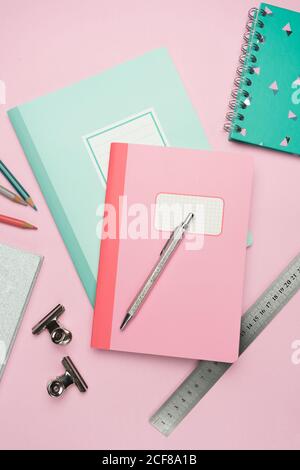 From above composition of colorful notebooks, pen, pencils, ruler and paper clips arranged on pink desk Stock Photo