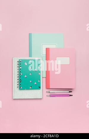 From above composition of colorful notebooks and paper clips arranged on pink desk Stock Photo