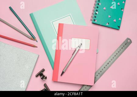 From above composition of colorful notebooks, pen, pencils, ruler and paper clips arranged on pink desk Stock Photo