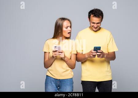 Portrait of couple with smart phones in hands, cheerful charming man checking her email, woman follows her secret correspondence with jealous expressi Stock Photo