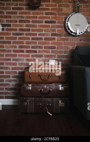 Old fashioned leather light and dark brown suitcases with metal locks put near brick wall with white cup above and hanging banjo in flat Stock Photo