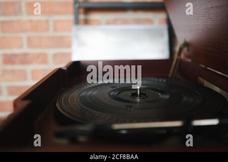 Closeup of record player with wooden lid having black vinyl record inside put near brick wall on blurred background Stock Photo