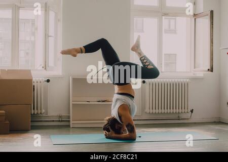 Side view of Woman in activewear exercising and doing headstand on floor in apartment Stock Photo