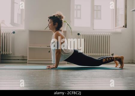 Side view of flexible Woman in activewear exercising and standing on hands on floor in apartment Stock Photo