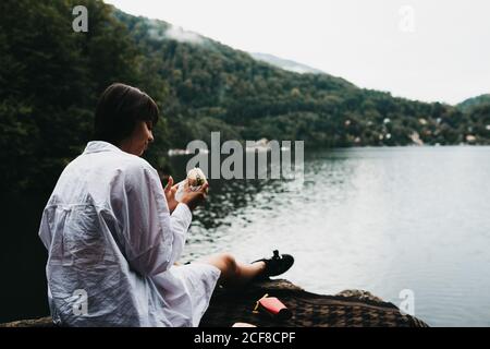 Woman eating hamburger near lake and mountains Stock Photo