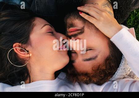 From above of cheerful young couple lying on plaid on green grass and enjoying time together while spending day in park Stock Photo