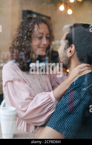 Side view of cheerful couple hugging in coffee shop drinking hot beverage and looking at each other Stock Photo