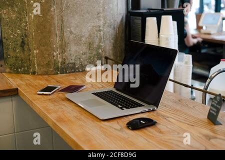 Modern netbook placed on wooden table with smartphone and mouse in cozy coffee shop Stock Photo