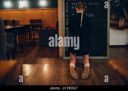 Young woman writing cafe menu on black desk chalkboard using chalk. Stock Photo