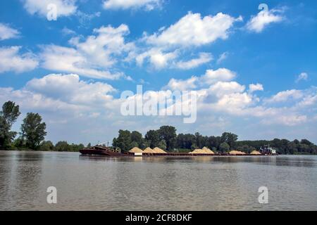 A large and powerful river boat pushes barges loaded with sand and gravel along the river. The ship sails powerfully in the middle of the river. Stock Photo