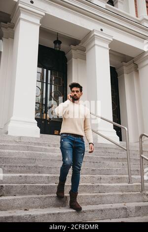 Stylish bearded man standing on stairs, talking by mobile phone outdoors Stock Photo