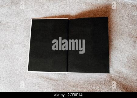 High angle of opened book with empty black pages on soft couch in light living room of modern apartment Stock Photo