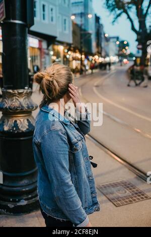 Side view of unrecognizable blonde Woman in casual outfit standing on street and looking away while getting ready crossing street Stock Photo