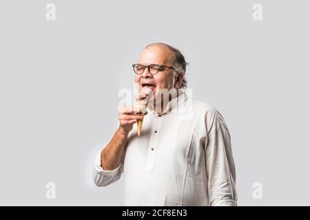 Indian Old man eating chocolate Ice cream in cone or mango candy bar Stock Photo