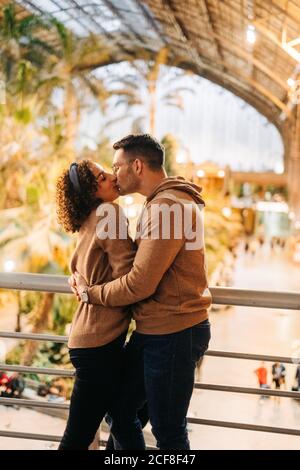 Cheerful young man and Woman embracing and kissing looking at each other while standing inside illuminated pavilion during date Stock Photo