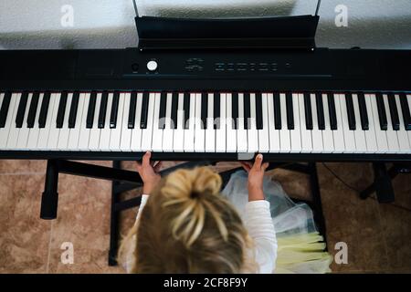 From above unrecognizable focused blond little girl playing synthesizer at home Stock Photo