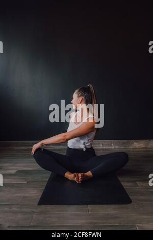 Diligent barefooted Woman in sportswear performing bound angle pose exercise on mat in light contemporary gym Stock Photo