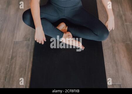 Diligent cropped unrecognizable barefooted Woman in sportswear performing bound angle pose exercise on mat in light contemporary gym Stock Photo