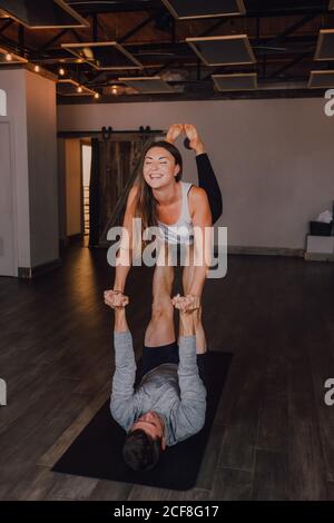 High angle of happy young barefooted couple in activewear looking at each other and smiling while doing balance exercise standing in front plank position on floor in contemporary studio Stock Photo