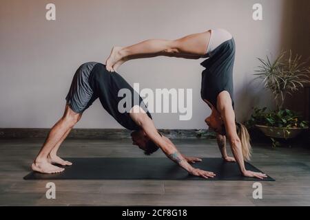 Side view of young barefooted man and focused Woman in sportswear doing balance exercise standing in dog pose while training together on floor in light contemporary workout room Stock Photo