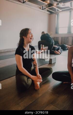 High angle of young diverse women and men in sportswear sitting in lotus pose and having interest discussions while resting after group training in contemporary yoga studio Stock Photo