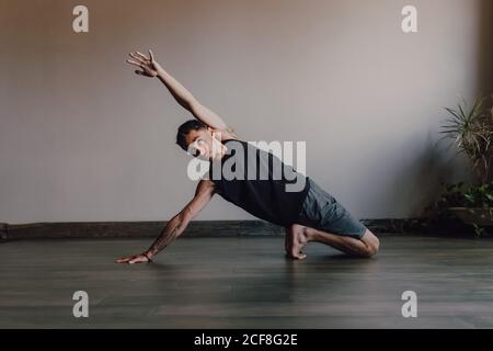 Diligent barefooted athlete in sportswear practicing yoga on wooden floor in spacious contemporary workout room Stock Photo