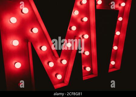 Huge M letter with red neon glowing bulbs on black wall in dark Stock Photo