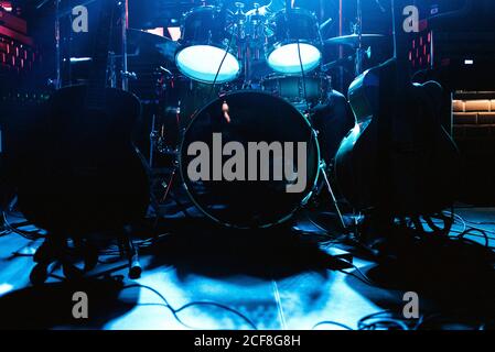 Large drum set with drums sticks and guitars on stage under blue neon light in anticipation of game Stock Photo