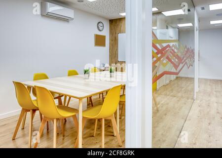 Light corridor with wooden floor among glass walls of light modern cozy office conference zones with comfortable yellow chairs at big wooden tables Stock Photo