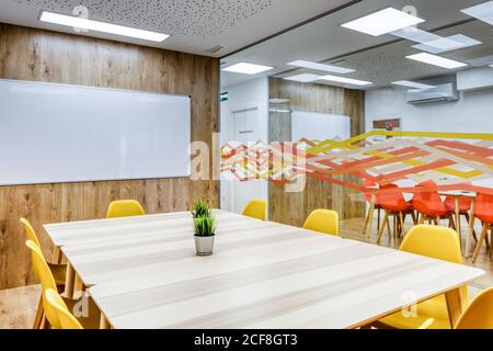 Modern interior design of light spacious office zoned by glass wall with comfortable yellow chairs and gray bar stools at wooden tables Stock Photo