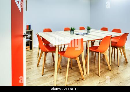 Modern interior design of light spacious office zoned by glass wall with comfortable orange chairs and gray bar stools at wooden tables Stock Photo