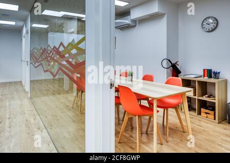 Light corridor with wooden floor among glass walls of light modern cozy office conference zones with comfortable orange chairs at big wooden tables Stock Photo