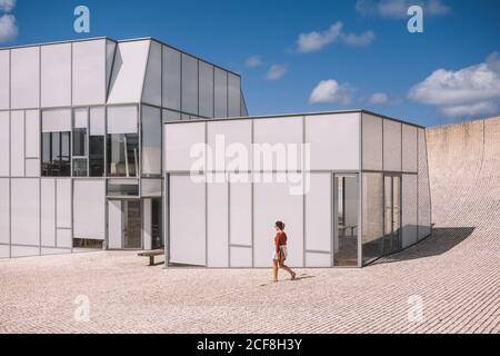 Female in casual wear waling near modern stylish building on block stone at empty area with blue sky on background Stock Photo