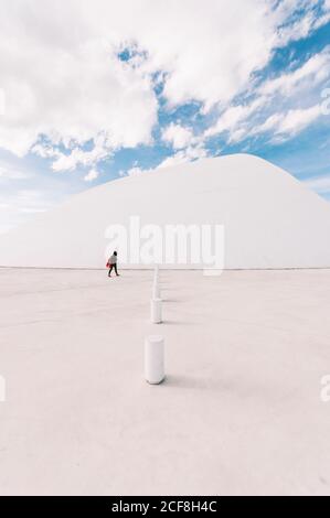 Unrecognizable person walking on empty square near white curved building of Oscar Niemeyer International Cultural Centre located in Asturias in Spain in sunny days with blue cloudy sky in background Stock Photo