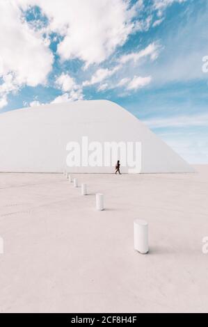 Unrecognizable person walking on empty square near white curved building of Oscar Niemeyer International Cultural Centre located in Asturias in Spain in sunny days with blue cloudy sky in background Stock Photo